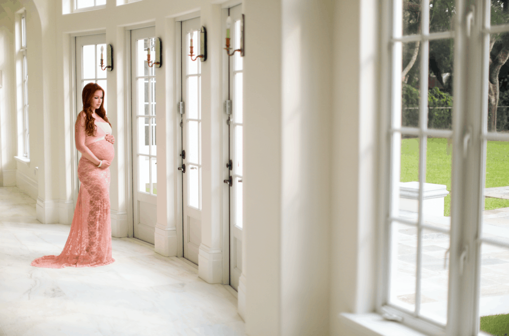 Home Maternity Shoot -  pregnant in pink lace dress in front of the windows for perfect lighting