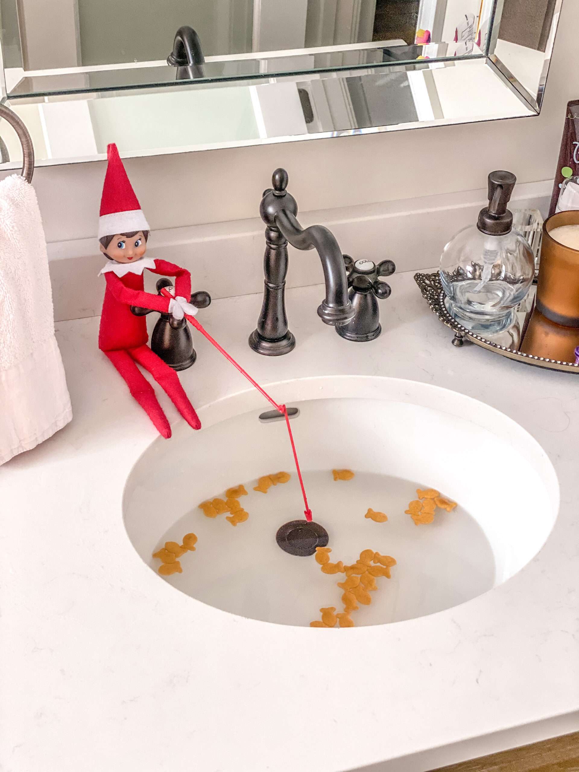 Fishing in the sink with goldfish crackers. Fun & easy Elf on the Shelf ideas for your toddler or little kid. Quick to setup and lots of naughty and nice ideas, perfect to bring some Christmas magic to your home. #ElfOnTheShelf #ElfIdeas #ElfOnTheShelfIdeas #Christmas #ChristmasMagic