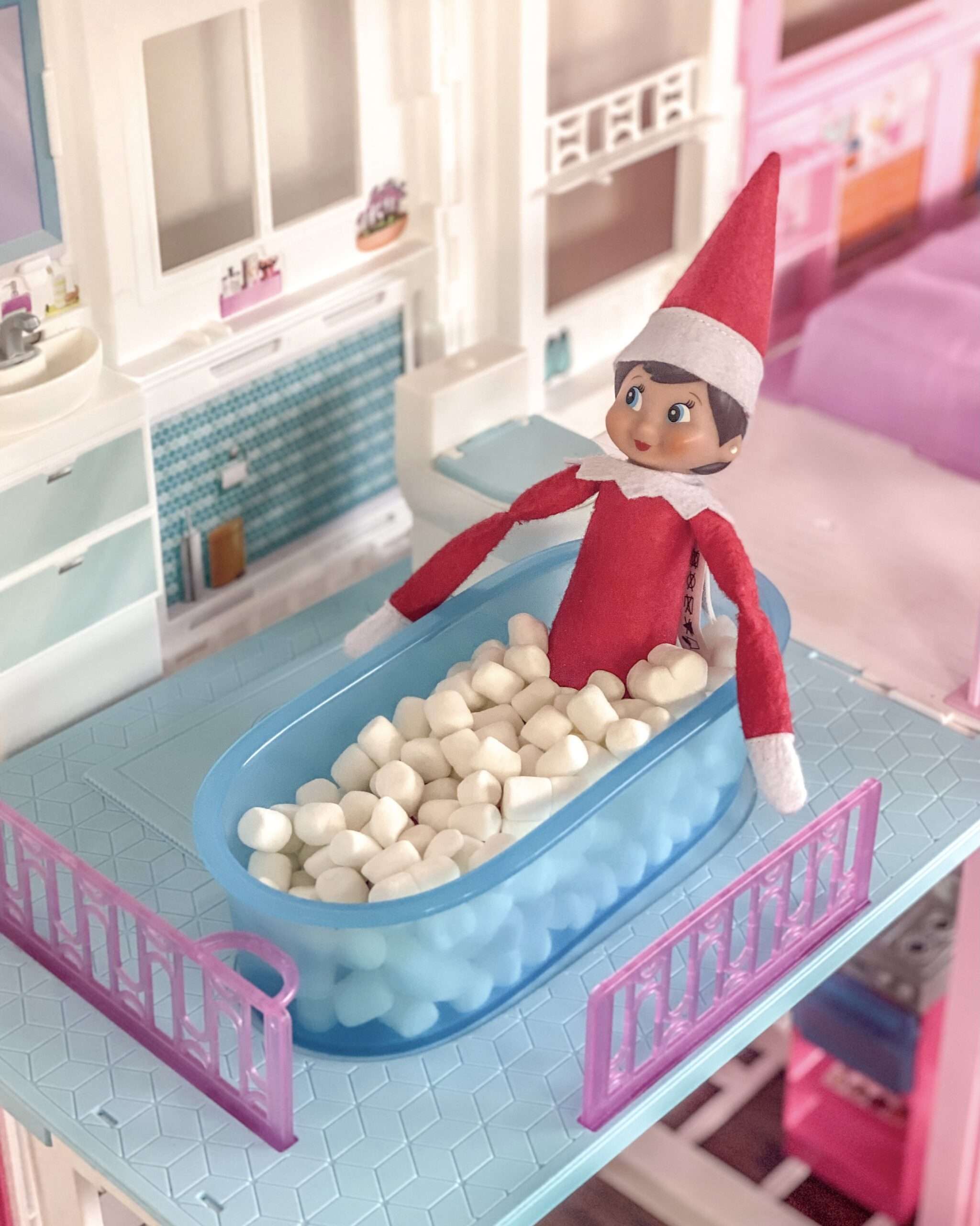 Mini Marshmallow bubble bath. Fun & easy Elf on the Shelf ideas for your toddler or little kid. Elf swinging on a roll of toilet paper. Quick to setup and lots of naughty and nice ideas, perfect to bring some Christmas magic to your home. #ElfOnTheShelf #ElfIdeas #ElfOnTheShelfIdeas #Christmas #ChristmasMagic