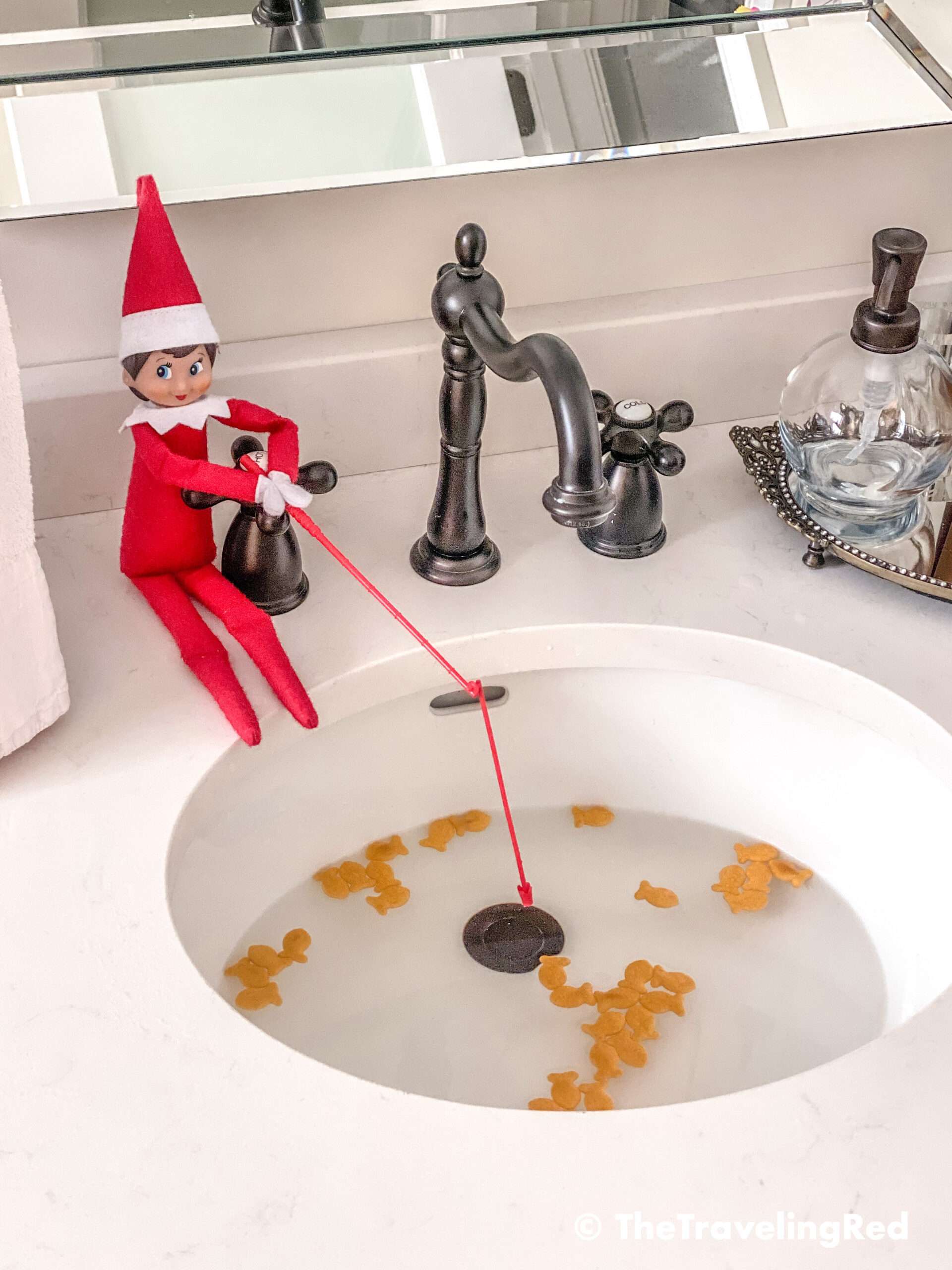 Naughty Elf on the shelf fishing in the sink for goldfish crackers. Fun and easy elf on the shelf ideas for a naughty elf that are quick and easy using things you have at home.