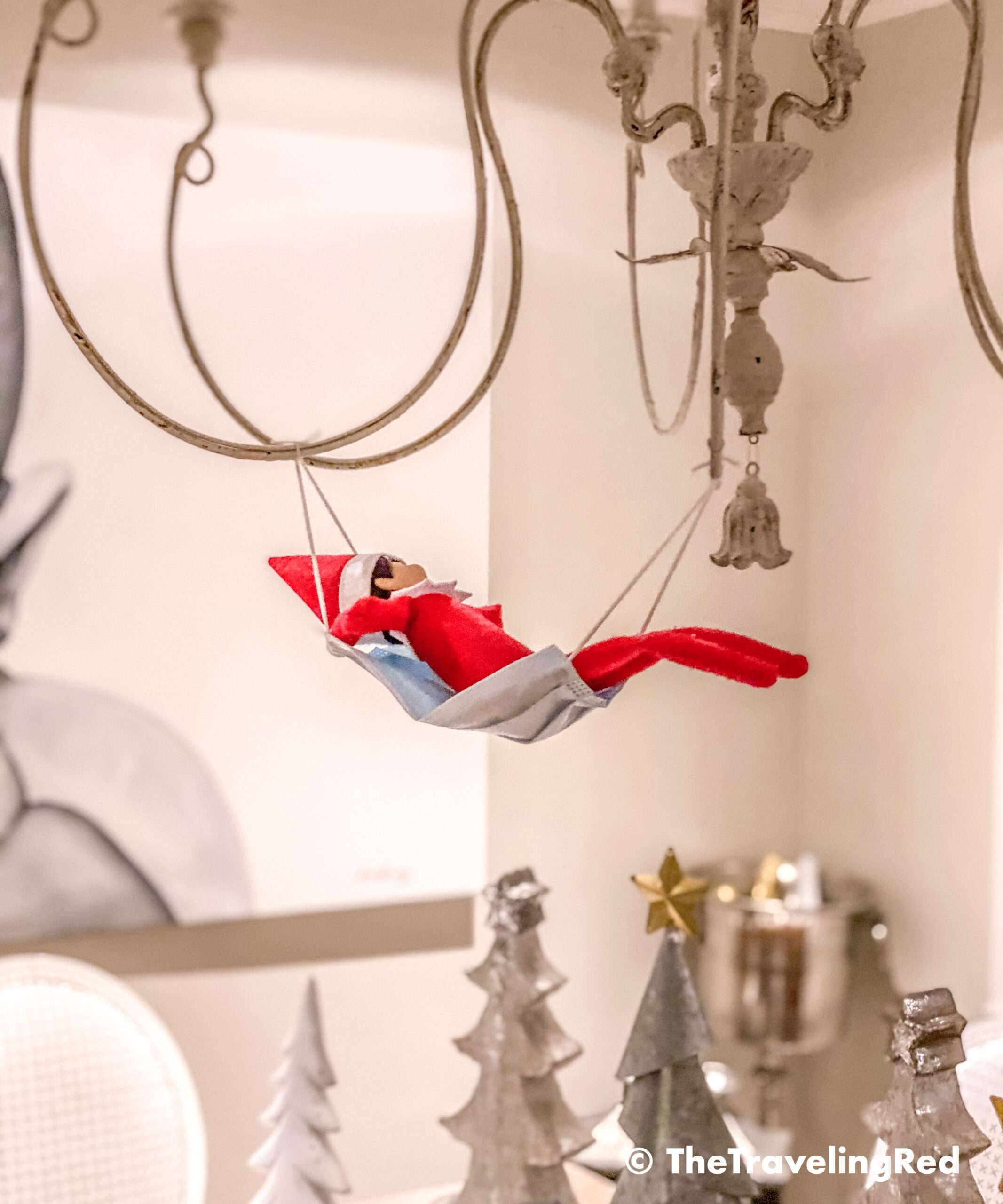 Naughty Elf on the shelf uses a disposable face mask as a hammock and put it on our chandelier. Fun and easy elf on the shelf ideas for a naughty elf that are quick and easy using things you have at home.